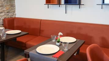 A modern dining area with a stone accent wall, orange seating, and a table set with plates and glasses.