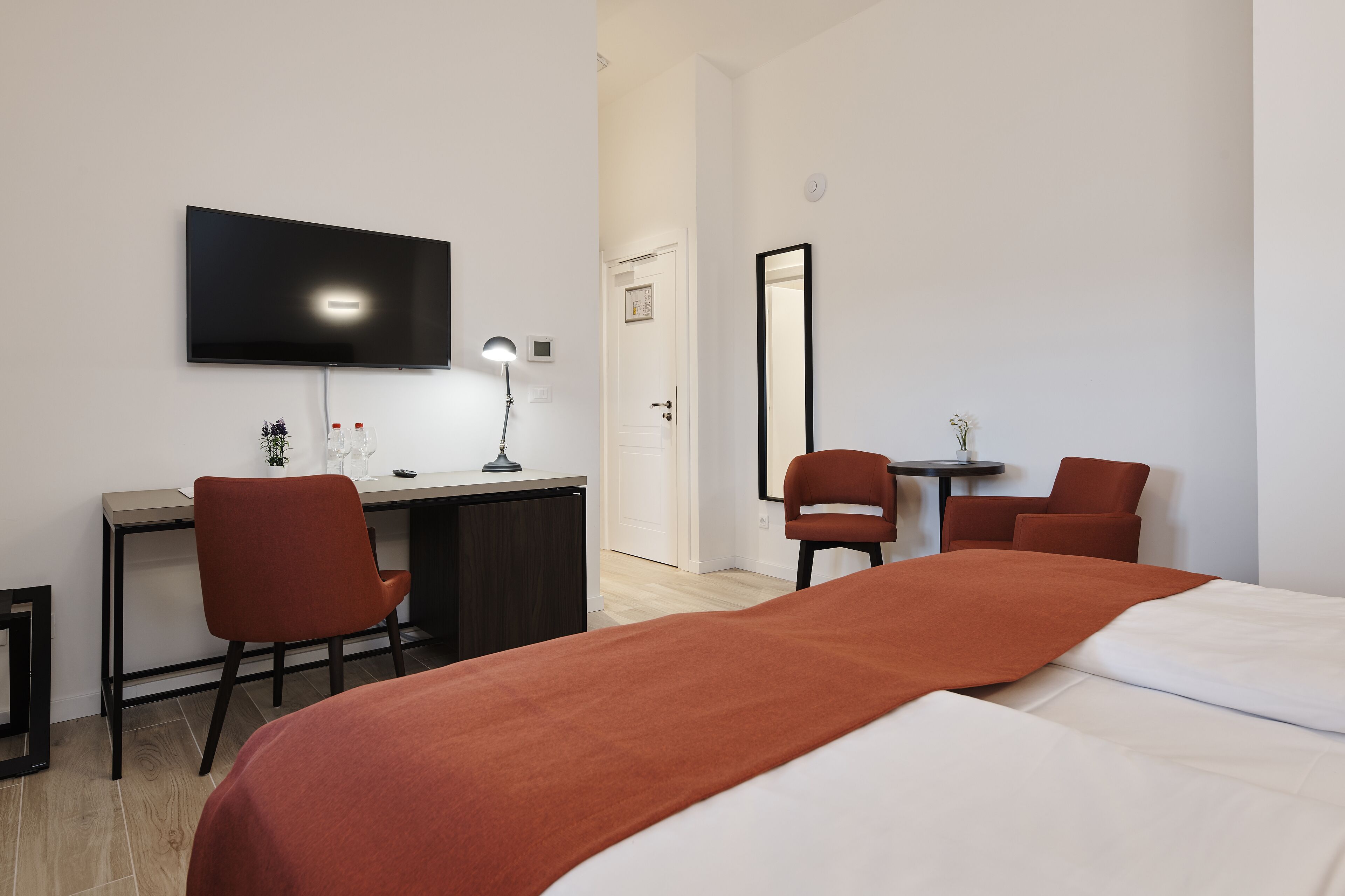 Ein Hotelzimmer mit einem Bett, einem Schreibtisch mit Stuhl, einem an der Wand befestigten Fernseher und einem Spiegel.
