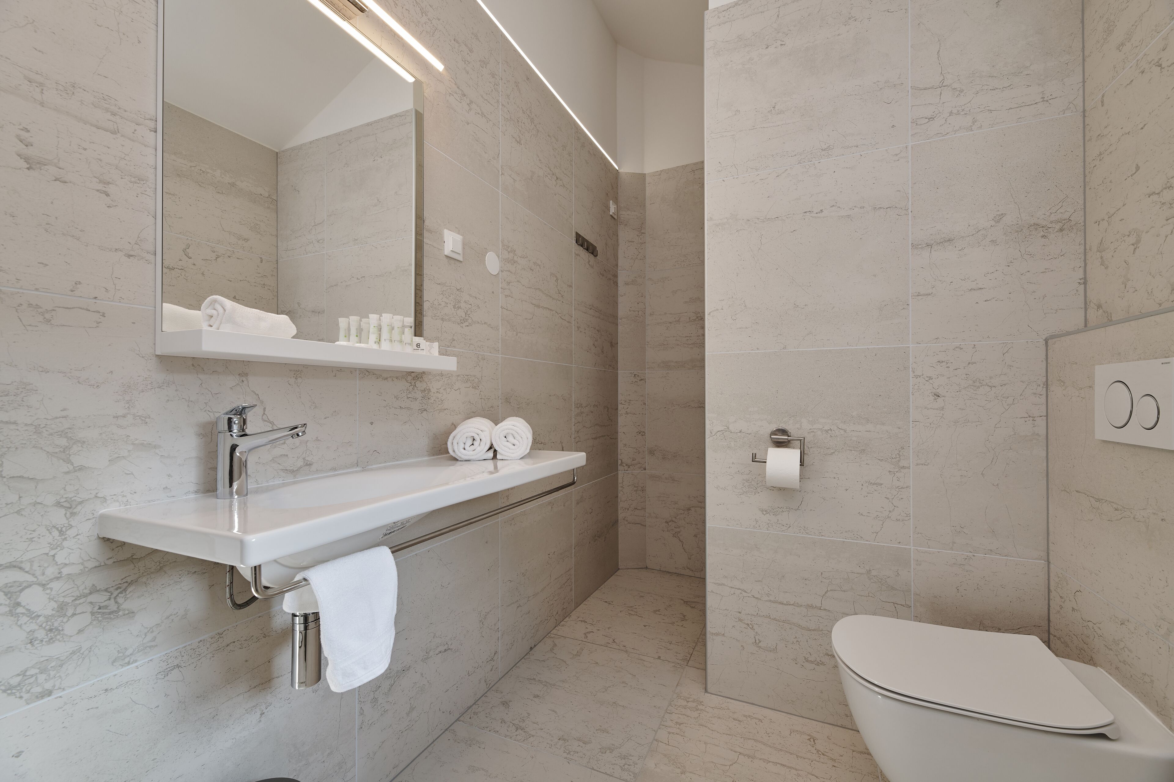 Un baño moderno con lavamanos, espejo y inodoro blancos.