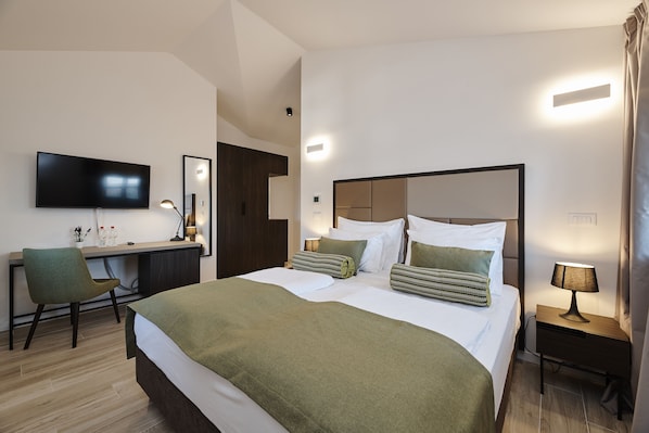 A hotel room with a large bed, a desk, a chair, a TV, and a nightstand with a lamp.