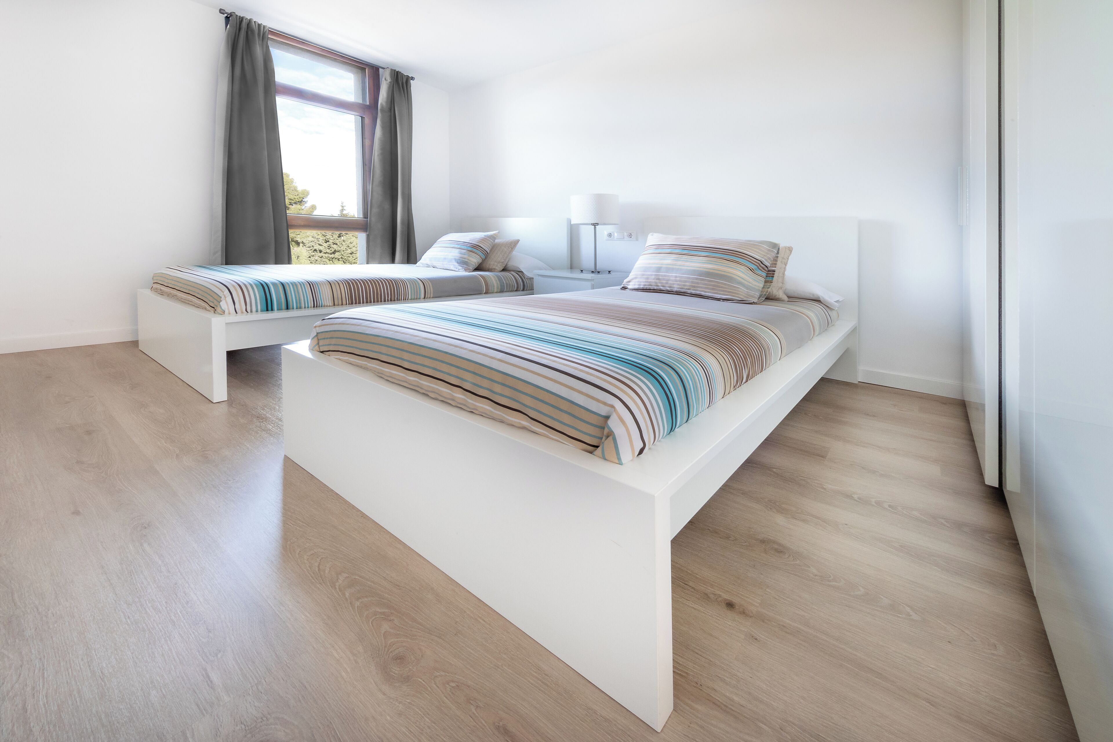 Een moderne slaapkamer met twee bedden, een groot raam en een bedlampje.
