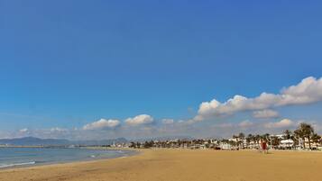 Ein weiter Sandstrand mit blauem Himmel und fernen Bergen.