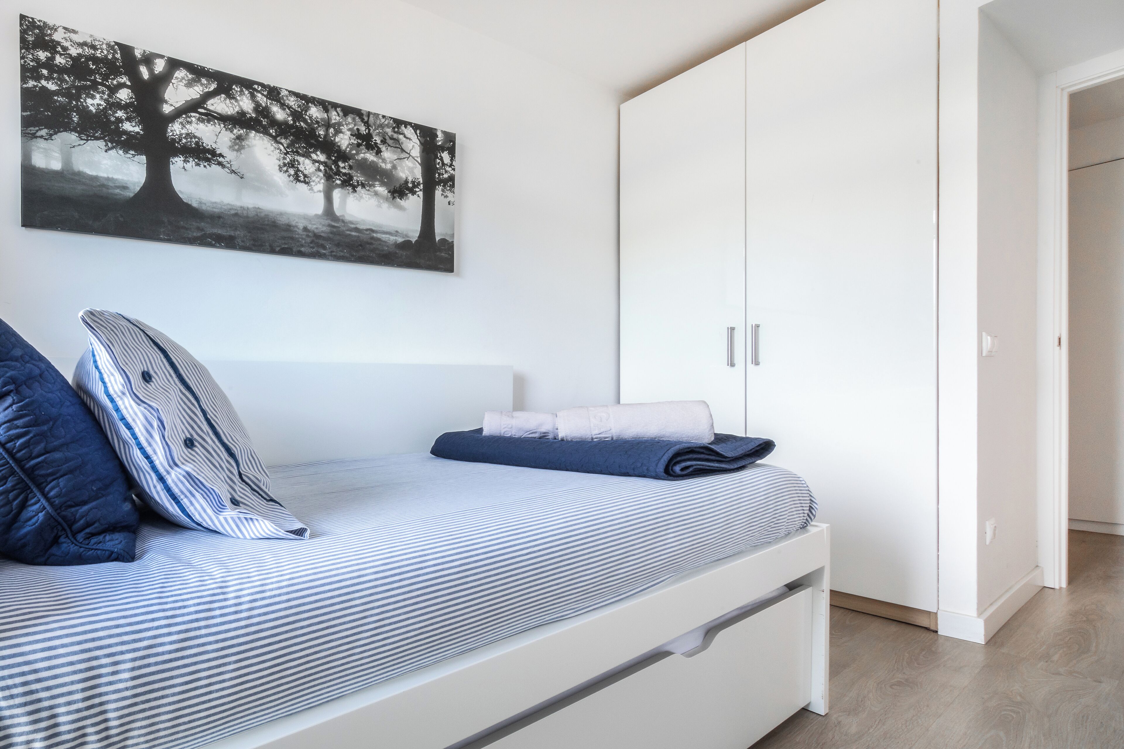 Een slaapkamer met een bed, kussens, een opgevouwen plaid, een kledingkast en een schilderij aan de muur.