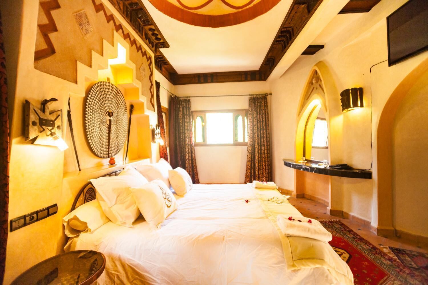 A hotel room with a large bed, a desk, a mirror, and a window with curtains.