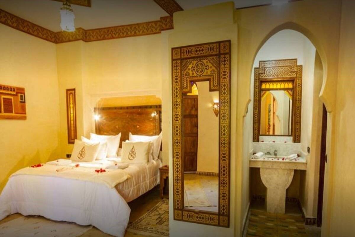 A hotel room with a large bed, a bathroom with a mirror and sink, and a decorative archway.