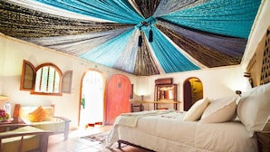 A bedroom with a large bed, a wooden chair, a small table, and a red door. - Riad Lamane (Zagora)