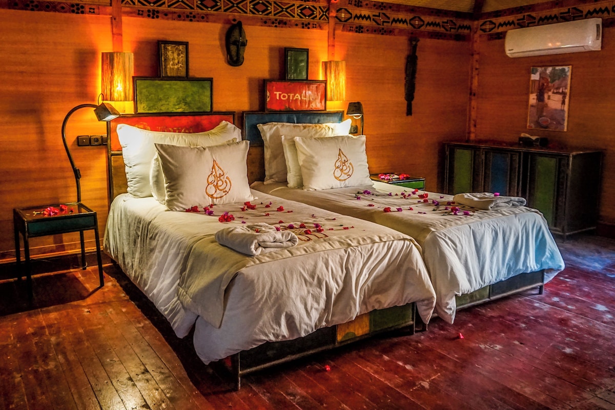 A room with two beds, a wooden floor, a wall with decorative patterns, and a wall-mounted air conditioner.