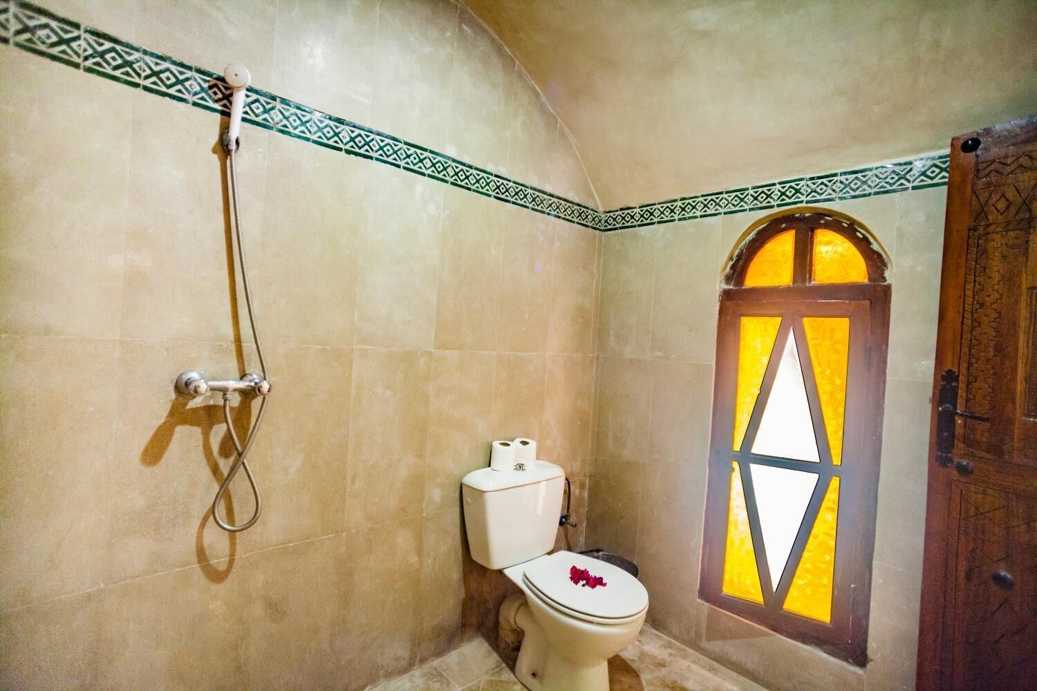 Een badkamer met een douche, toilet en een raam met een geometrisch ontwerp.