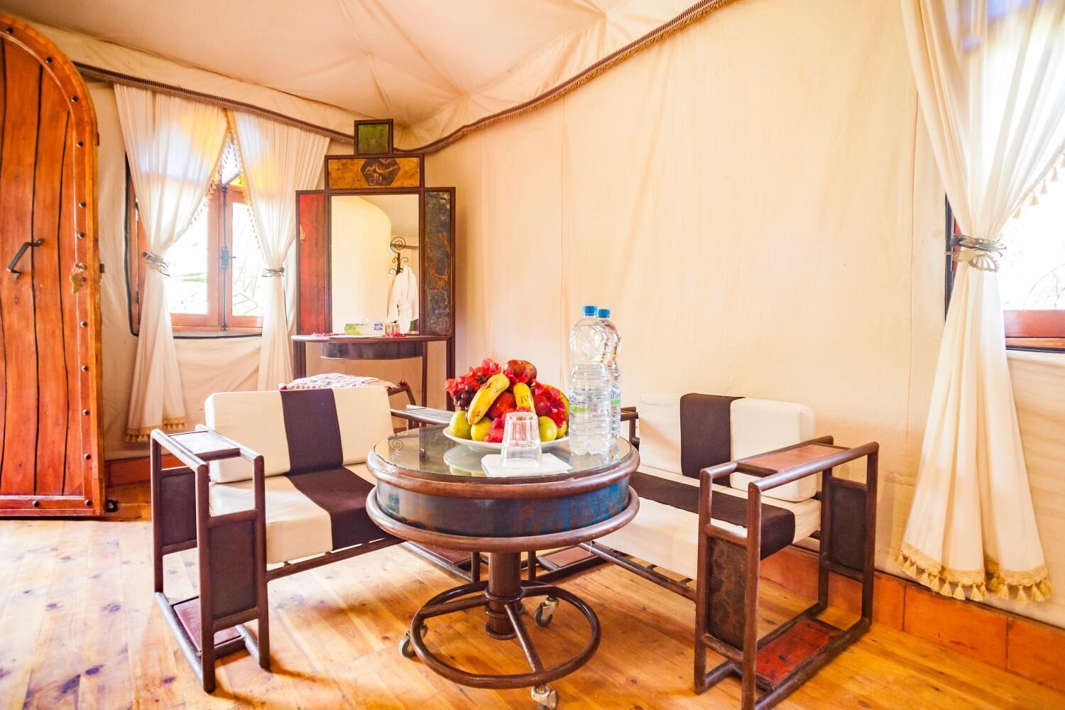 A tented room with a round table, chairs, a mirror, and a fruit bowl.