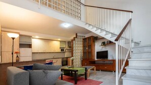 Un amplio salón con un sofá gris, una mesita y una escalera que sube a un nivel superior.