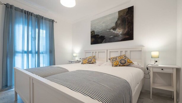 Un dormitorio con una cama grande, dos mesitas de noche, un cuadro en la pared y una ventana con cortinas.