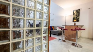 Una sala de estar moderna con un separador de vidrio, un sofá gris, dos taburetes altos y un cuadro en la pared.