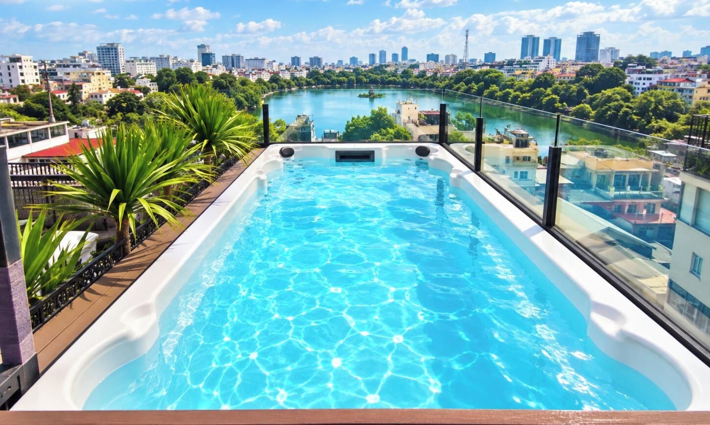 Une piscine à débordement située sur le toit, offrant une vue sur la ville, entourée de verdure et dotée d’une balustrade en verre.