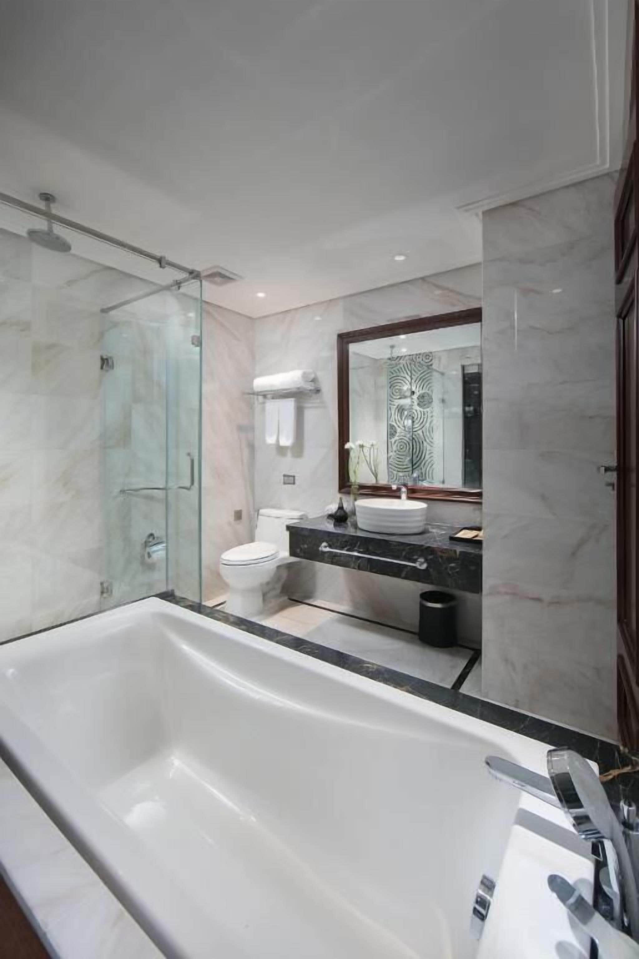 Ein modernes Badezimmer mit einer großen Badewanne, einer Duschkabine aus Glas, einer Toilette und einem Waschtisch mit Spiegel.