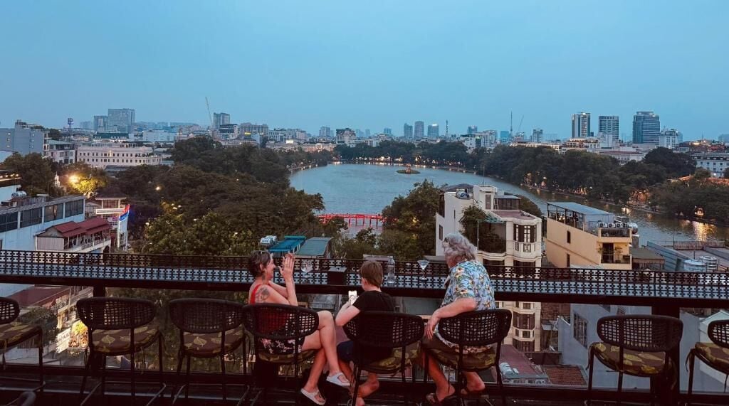 Un balcon avec trois chaises donnant sur un paysage urbain comprenant une rivière, des bâtiments et un pont.
