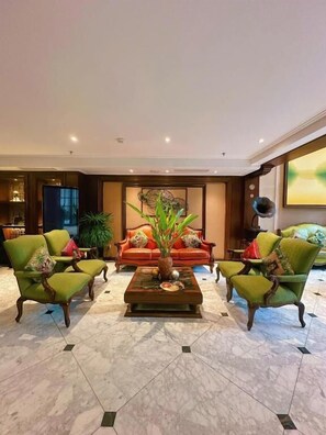 A spacious lobby with a marble floor, a red sofa, green armchairs, and a coffee table with a vase.