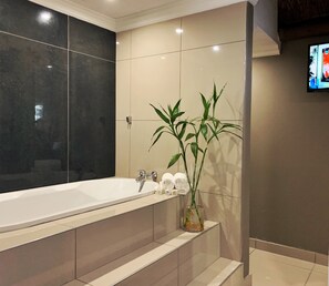 Une salle de bain moderne avec une grande baignoire blanche, une petite plante et des serviettes soigneusement pliées sur le comptoir.
