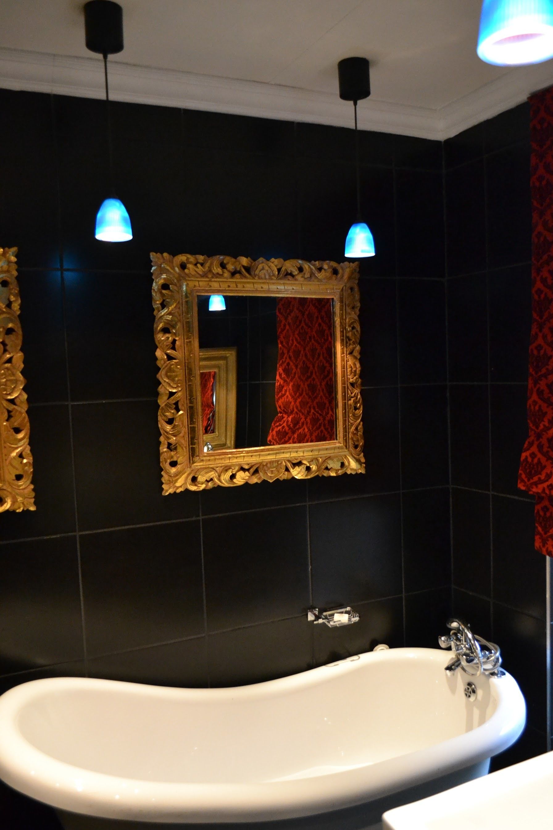 A bathroom with a freestanding bathtub, a large mirror with an ornate frame, and two pendant lights.