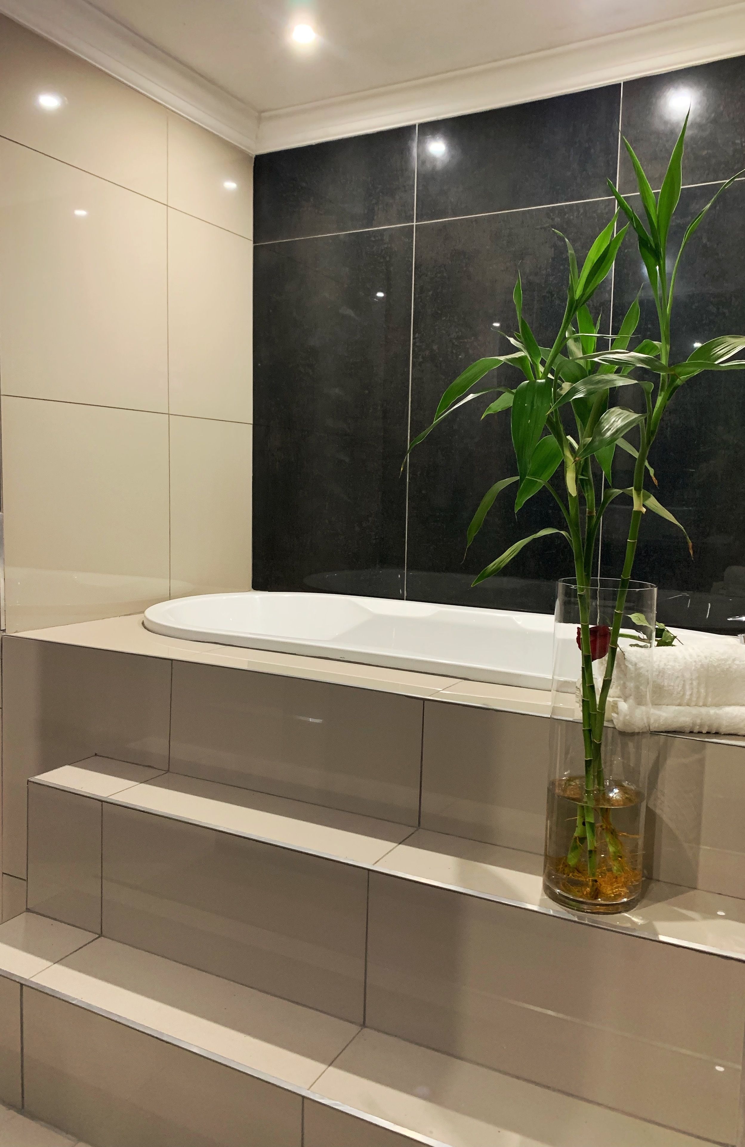 Un baño moderno con una bañera, un florero de vidrio con una planta y una toalla sobre el borde.