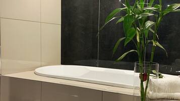 Un baño moderno con una bañera, un florero de vidrio con una planta y una toalla sobre el borde.