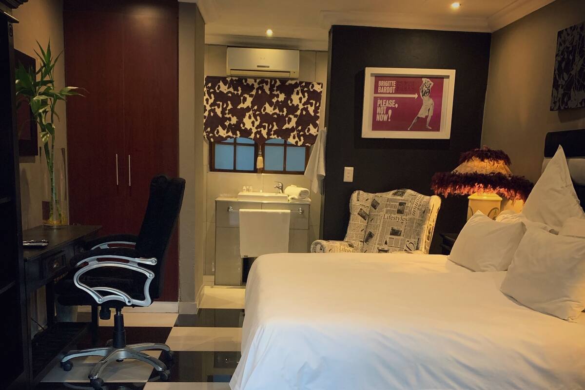 Une chambre d’hôtel moderne avec un sol à carreaux, un grand lit, un bureau, une chaise, une coiffeuse avec un miroir et un climatiseur fixé au mur.