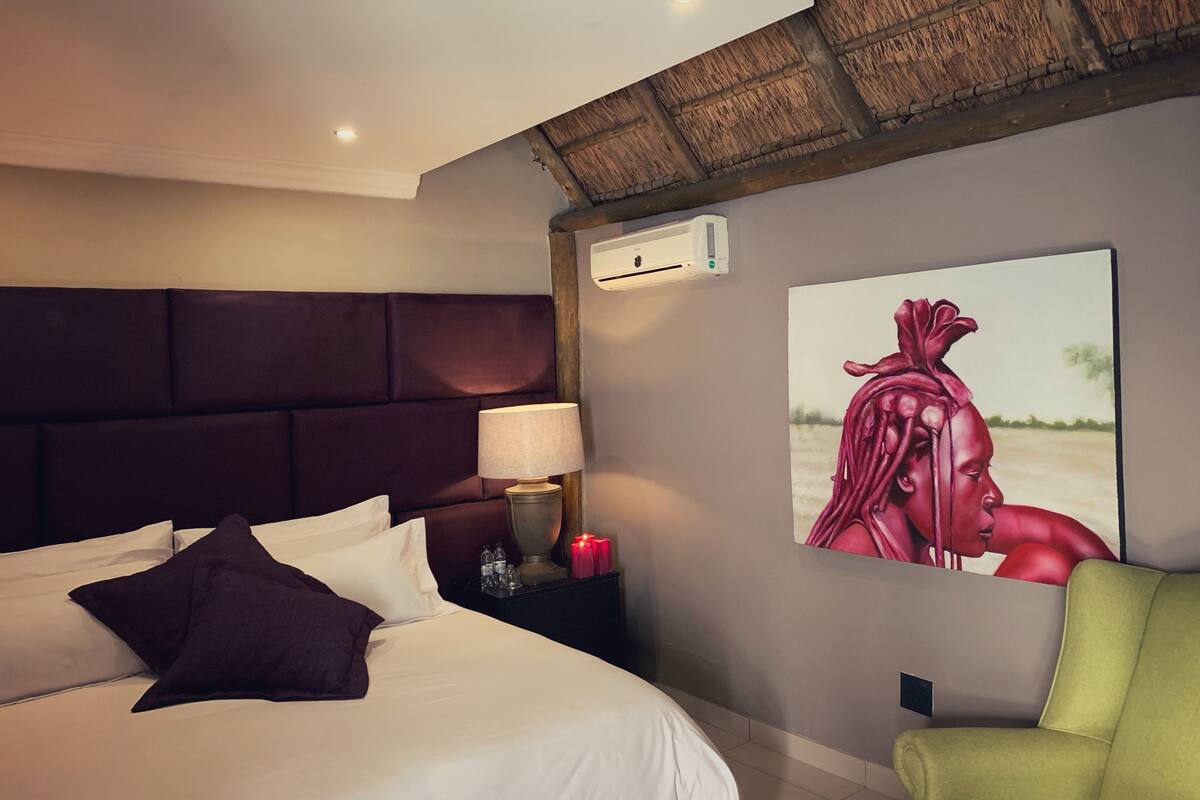 Une chambre d’hôtel avec un grand lit, une tête de lit, une table de chevet avec une lampe, un tableau au mur et un fauteuil vert.