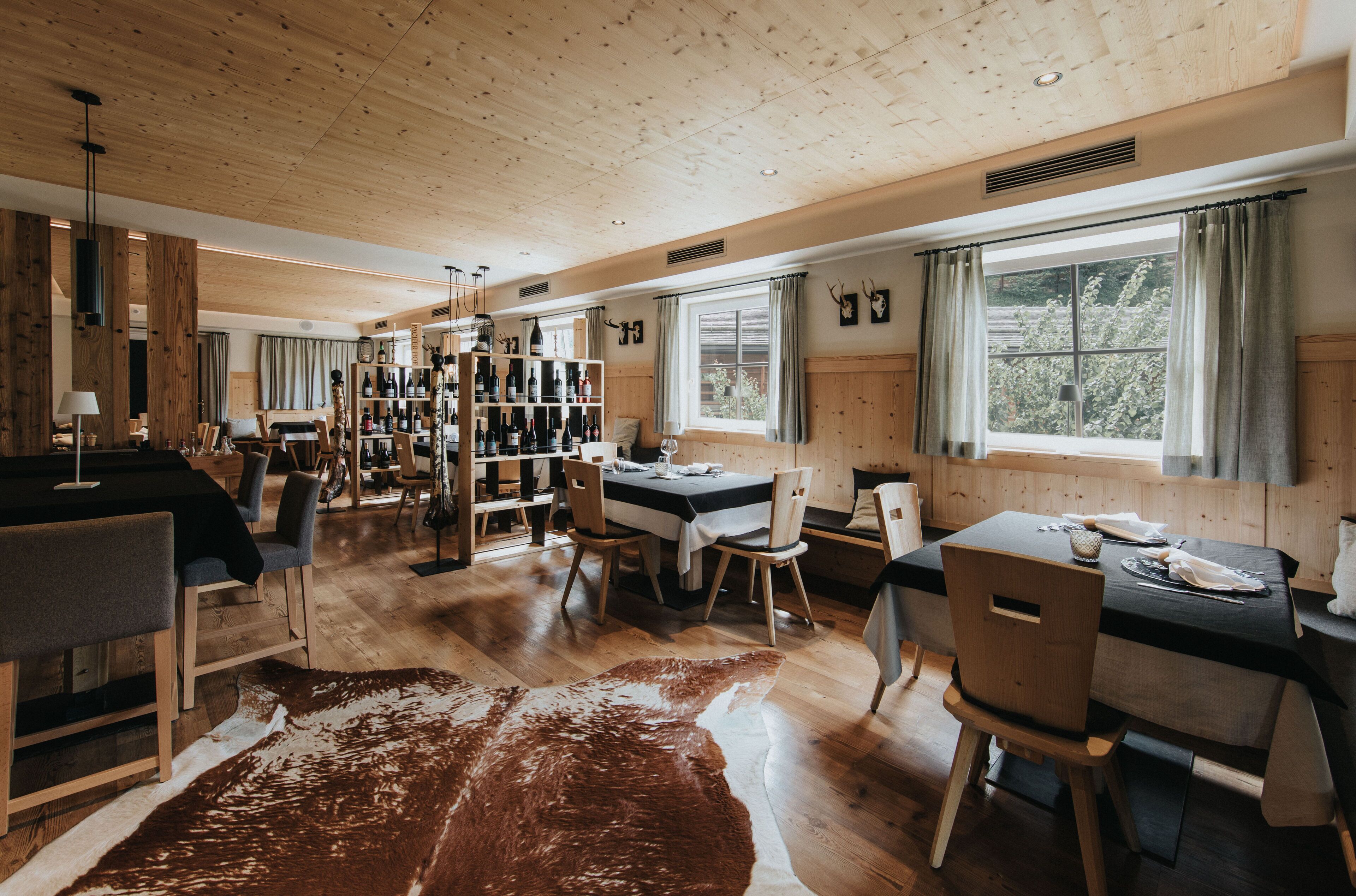 A spacious room with wooden floors, a dining area, a bar with shelves of bottles, and a large window with curtains.