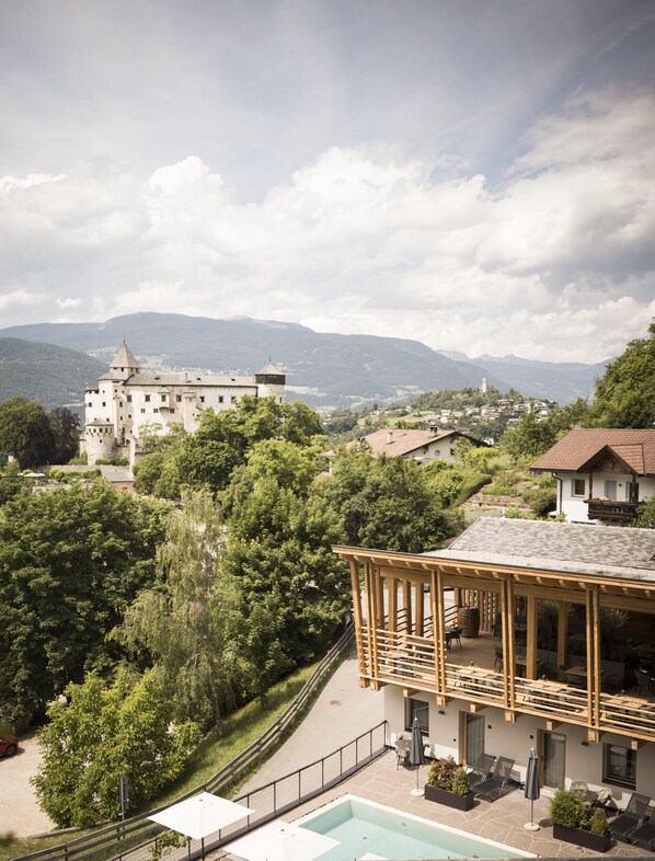 A hotel with a pool, outdoor seating, and a view of a castle and mountains.