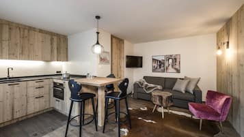 Una cocina moderna con armarios de madera, un comedor con taburetes, un sofá gris, una silla roja y una pequeña mesa de madera.