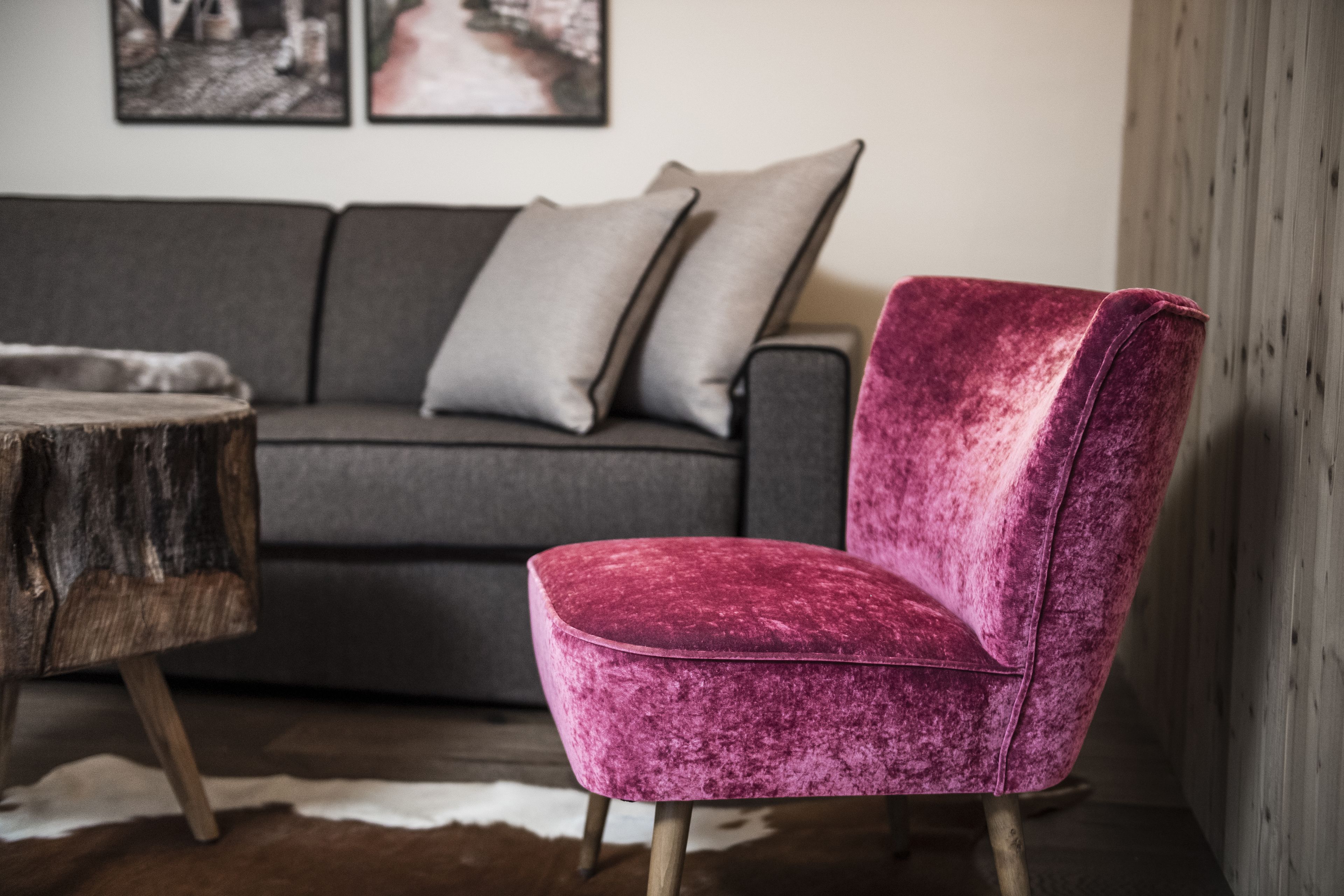 A room with a grey sofa, a pink velvet chair, and a wooden table.