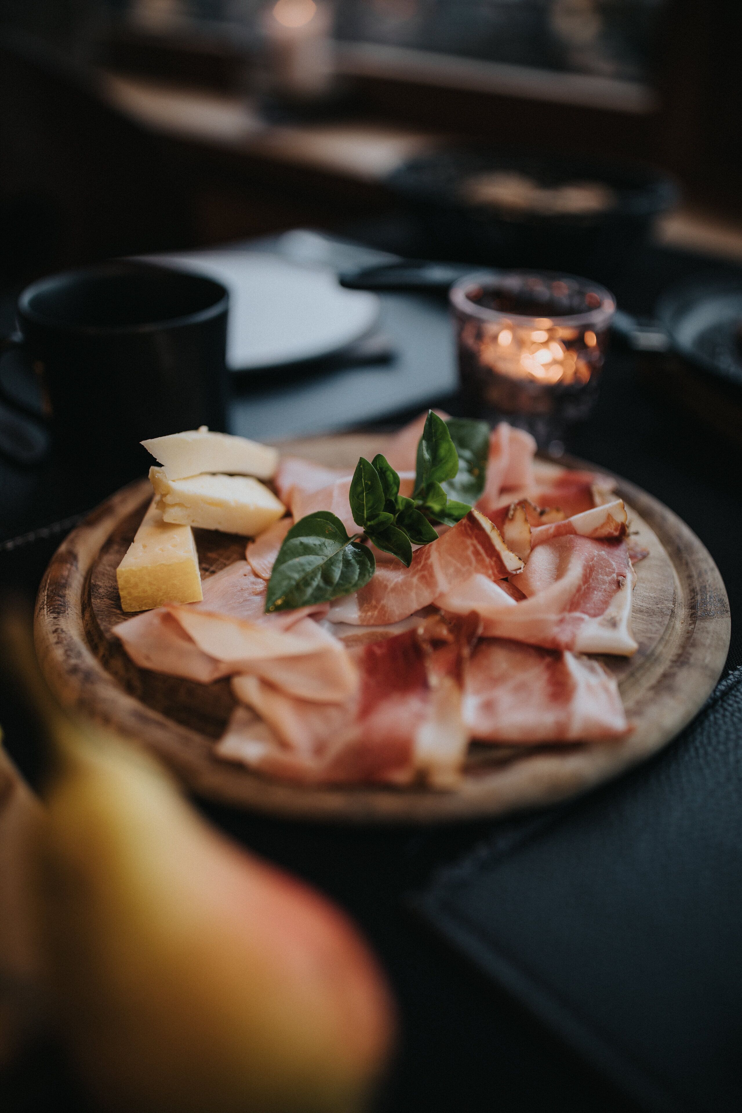 Una tabla de madera con fiambres, queso y una ramita de verdura como adorno.