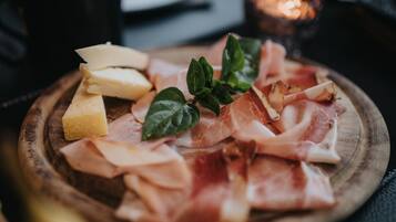 Una tabla de madera con fiambres, queso y una ramita de verdura como adorno.