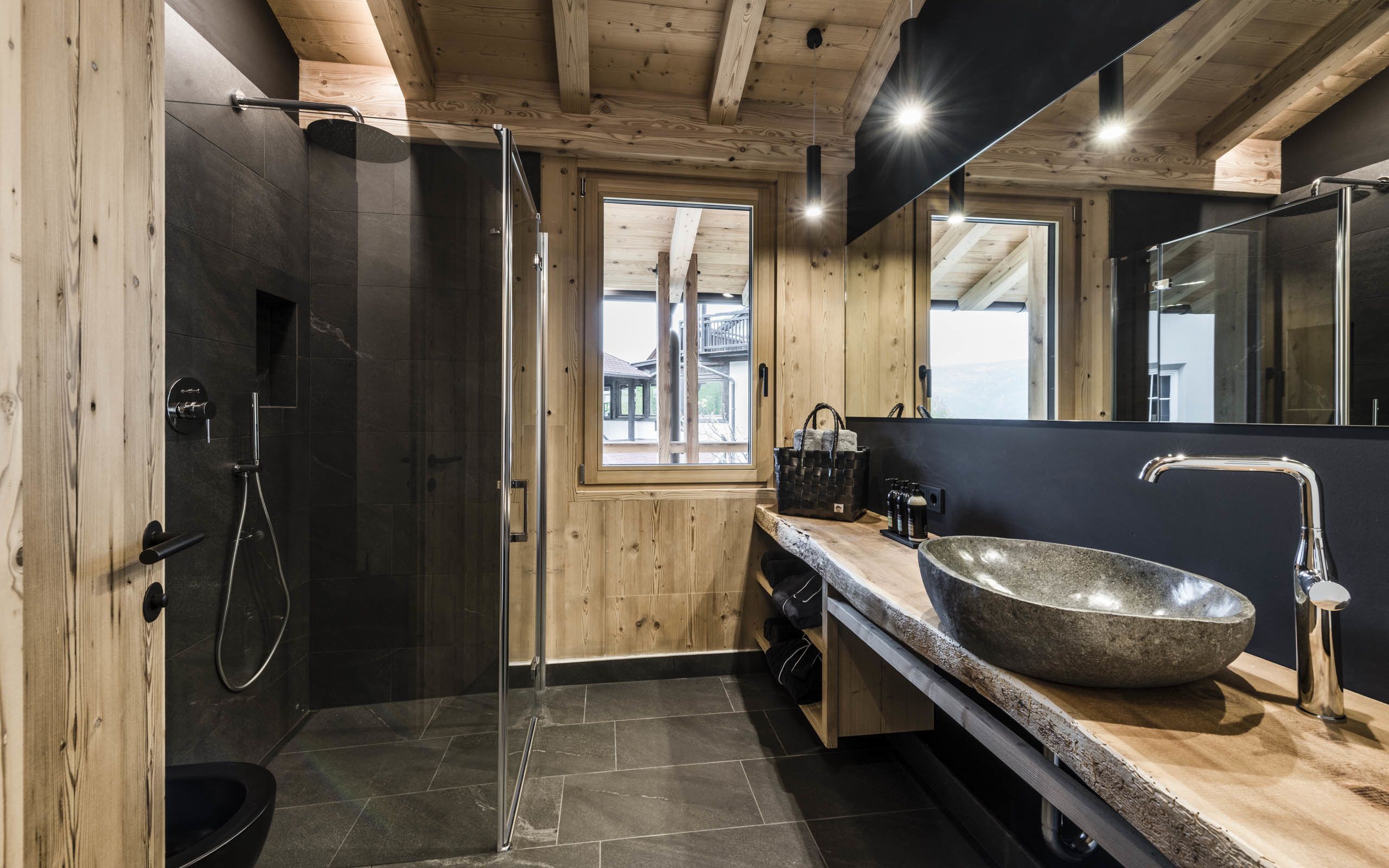 Une salle de bain moderne avec un lavabo en pierre, une douche à parois de verre, des murs en bois et un grand miroir.