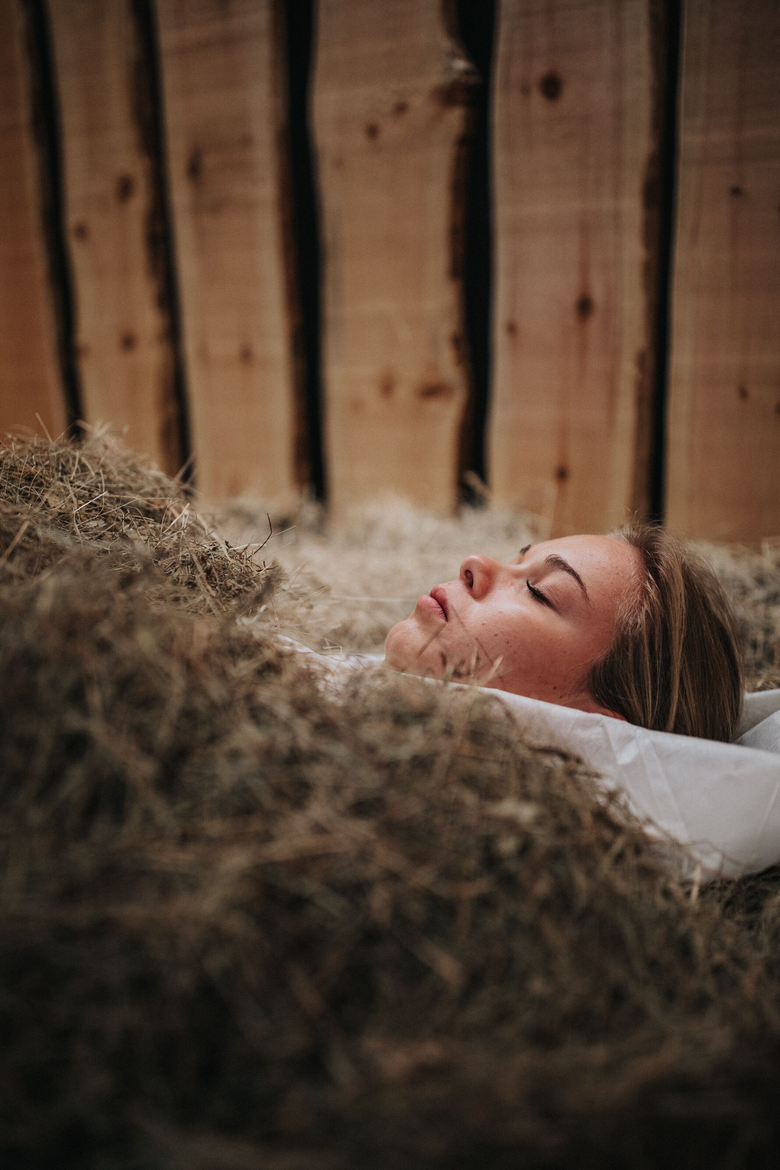 A person lying on hay in a rustic setting with wooden walls.
