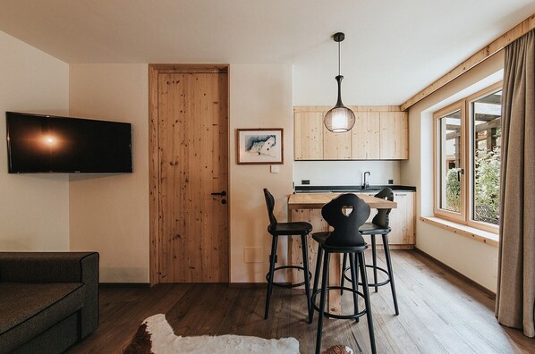 A compact living space with a kitchenette, a flat-screen TV mounted on the wall, a wooden door, and a window with curtains.