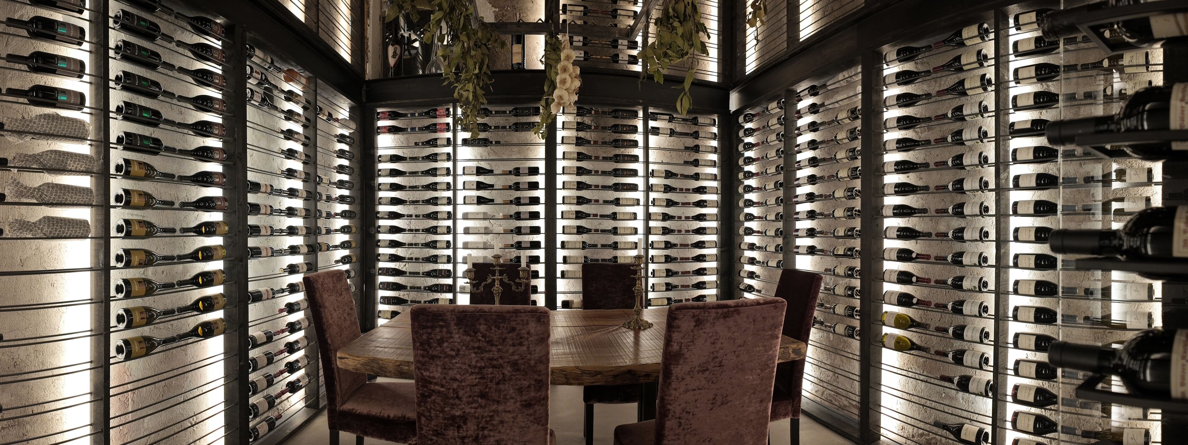 Una bodega con hileras de botellas de vino en estantes, una mesa de madera y sillones de terciopelo.