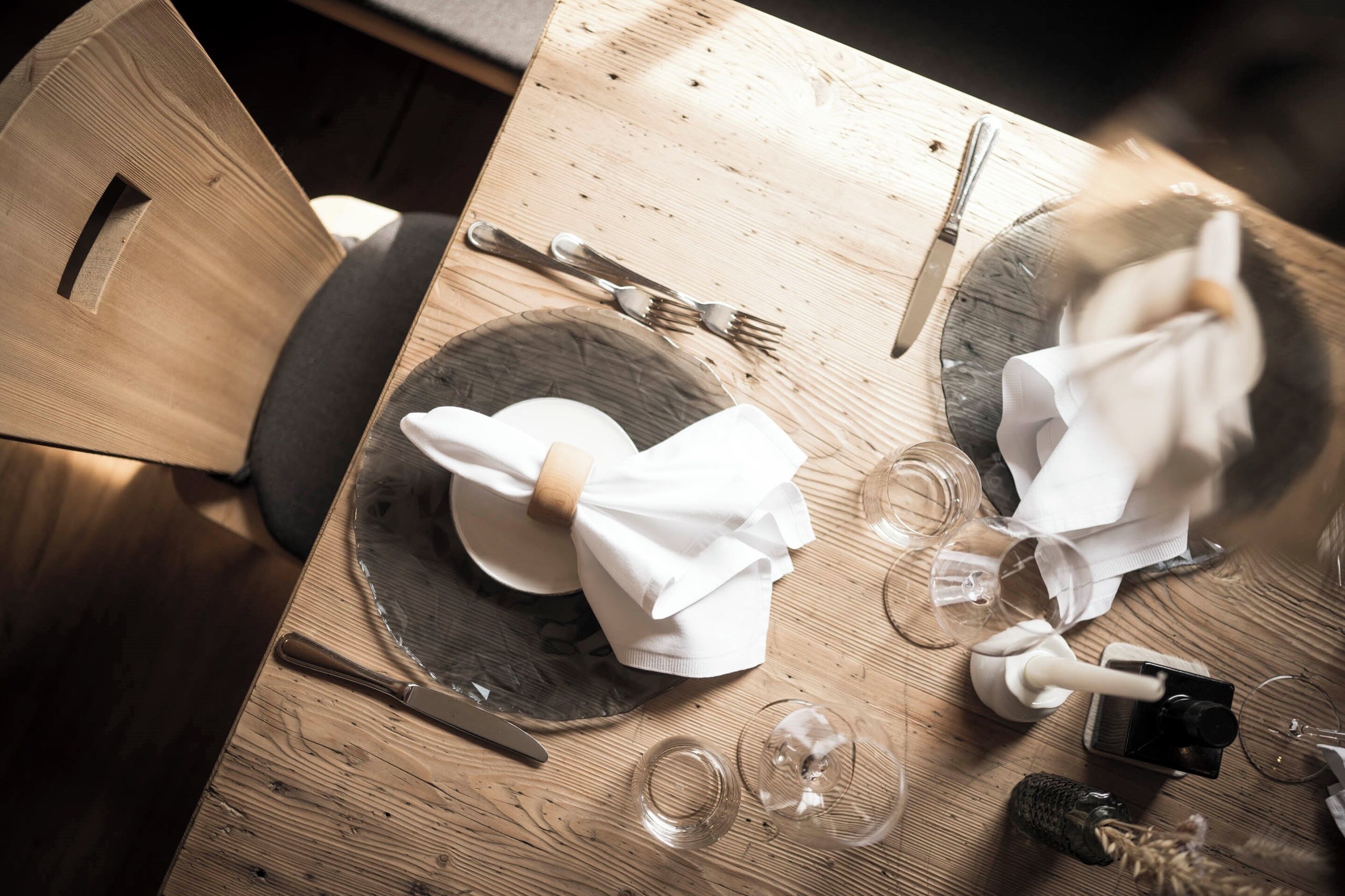 A wooden dining table with plates, cutlery, and glasses.
