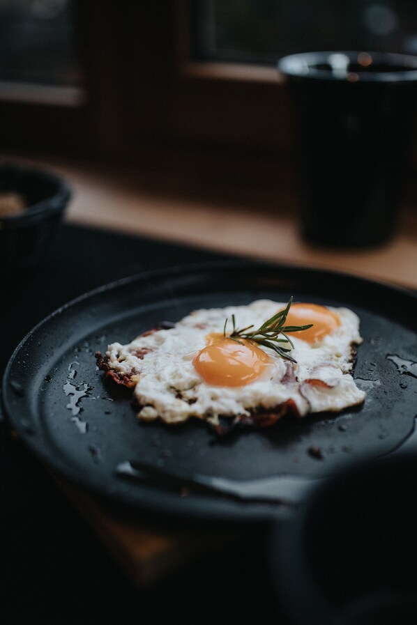 A close-up of a cooked egg on a black skillet with a sprig of rosemary on top. - Presulis Hideaway Apartments & Restaurant (Fie allo Sciliar)