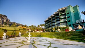 A hotel with a modern design, featuring a central courtyard with a fountain, surrounded by well-manicured lawns and a mountain backdrop. - Apartment in Aonang & Railay Sea View (Krabi)