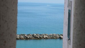 Une vue sur la mer, prise à travers une fenêtre, avec une barrière en pierre au premier plan.