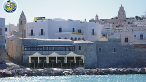 Une ville côtière qui se distingue par un imposant bâtiment blanc portant l’inscription « Rocca sul Mare » et un panneau indiquant « Chambre d’hôtes ».