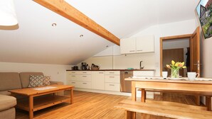 Un apartamento estilo loft acogedor, con piso de madera, una mesa de comedor, un sofá y una kitchenette al fondo.