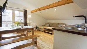 Una sala acogedora con sofá, una mesa de comedor con bancos, una zona de cocina con lavabo y una ventana con cortinas.