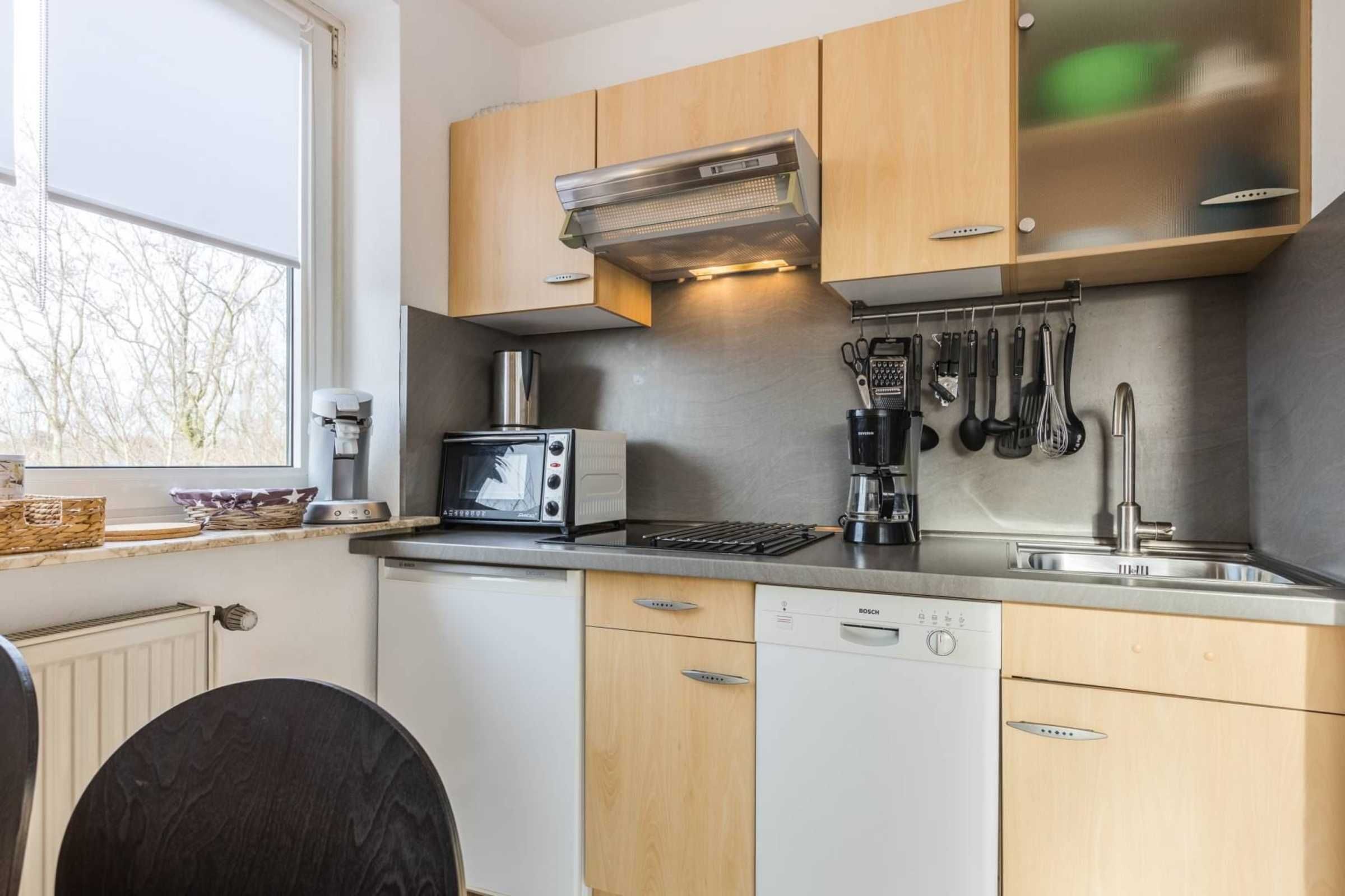 Una cocina compacta con armarios de madera, un lavavajillas Bosch, un microondas y una cafetera.