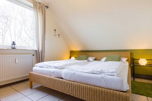 A bedroom with a large bed, two bedside tables, a window with curtains, and a radiator.
