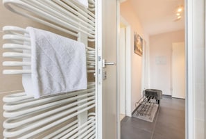 Un baño con toallero blanco, puerta de ducha de cristal y suelo de baldosas.