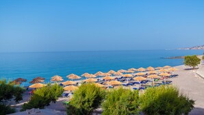 Ein Strand mit Reihen von Sonnenschirmen und Liegestühlen, ein klarer, blauer Himmel und das Meer im Hintergrund.