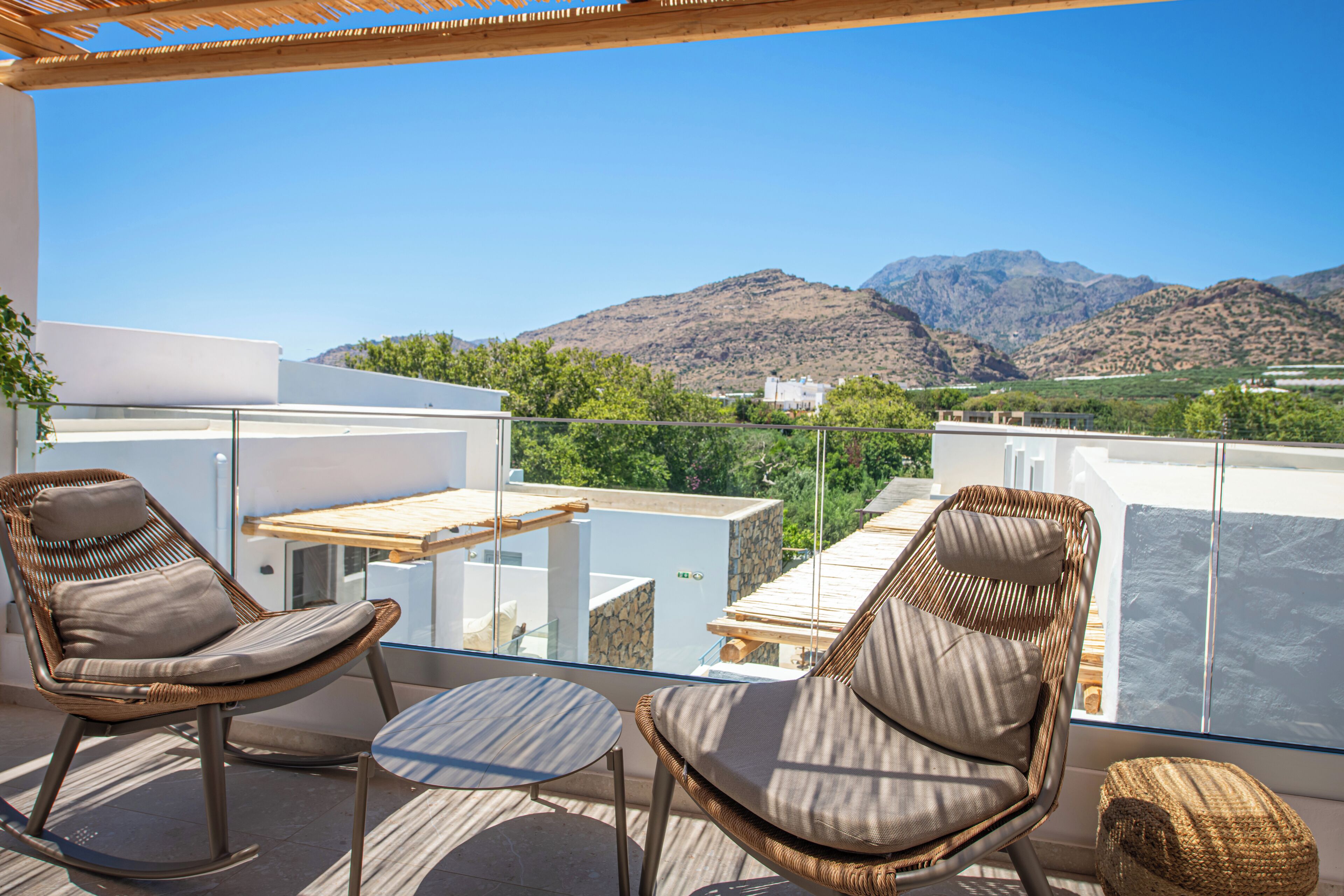 A balcony with wicker chairs, a small table, and a view of mountains.