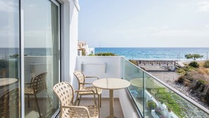 Ein Balkon mit Glastür, Korbstühlen, einem kleinen runden Tisch und Blick aufs Meer.