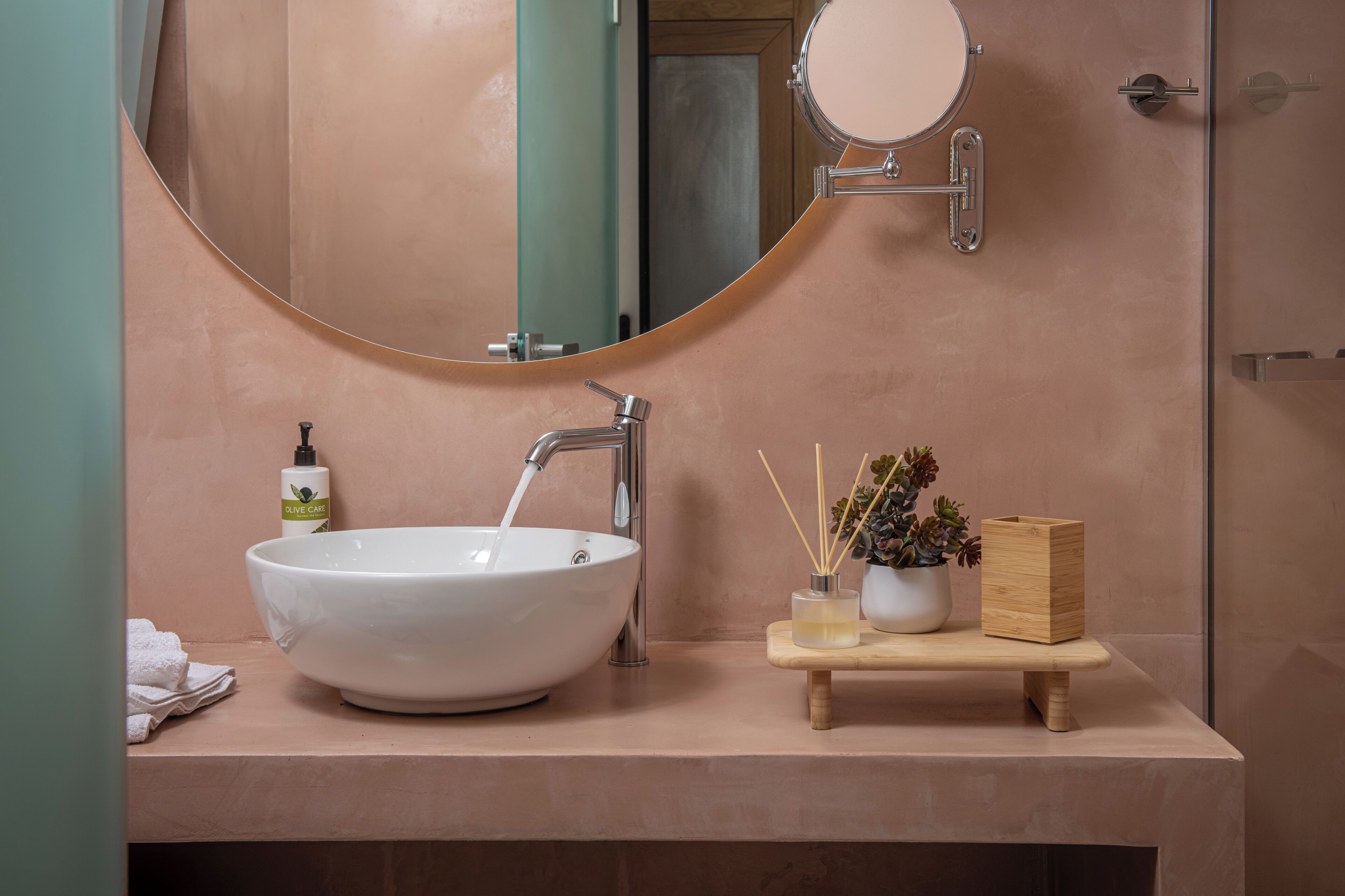 A bathroom with a large white sink, a mirror, a bottle of olive oil, and a small plant on a wooden tray.
